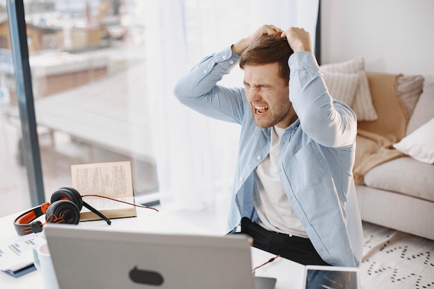 Man sitting in living room at home. Guy enjoying studying using laptop and headset. Angry.