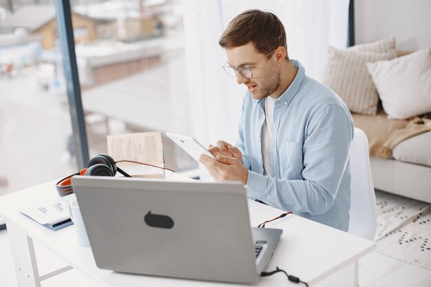 自宅の居間に座っている男。ノートパソコンとヘッドセットを使用して勉強を楽しんでいる男。男はタブレットを使用します。