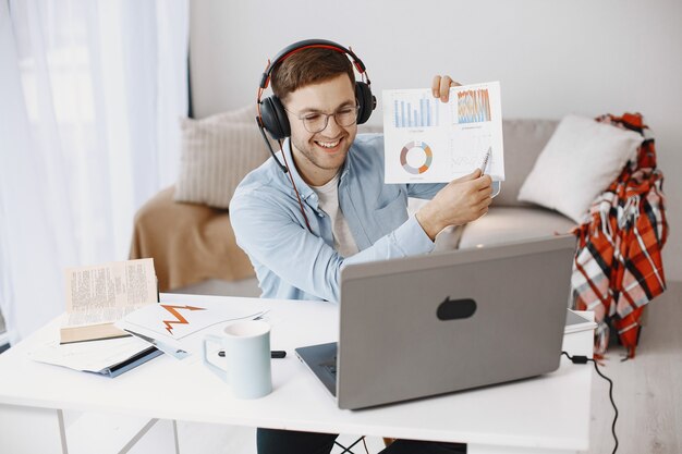 집에서 거실에 앉아 있는 남자. 노트북과 헤드셋을 사용하여 공부를 즐기는 남자.