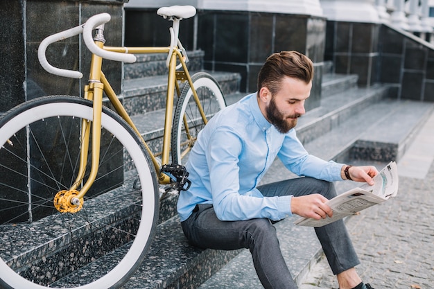 Man sitting near bicycle and reading newspaper