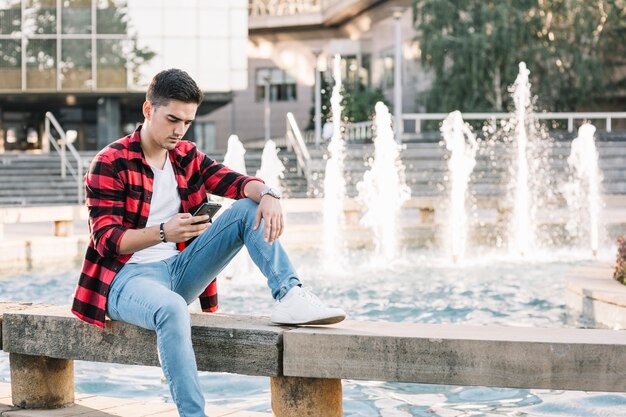 Man sitting near fountain using cellphone