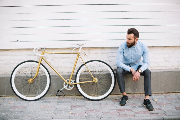 白い壁と自転車の近くに座っている男