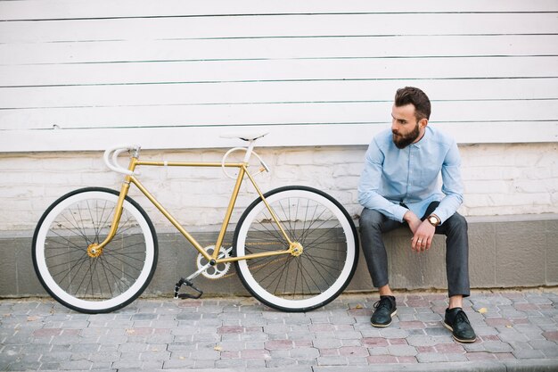 Человек сидит возле белой стены и велосипеда
