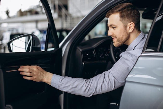 Free photo man sitting in new car in a car showroom