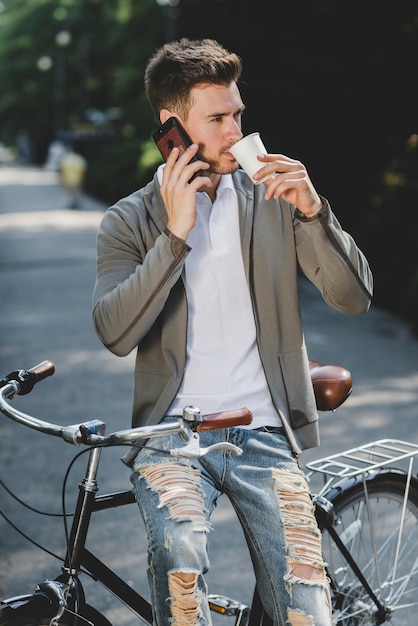 無料写真 携帯電話で話す自転車に座っている男コーヒーを飲む