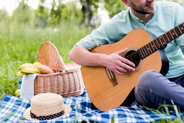 Free photo man sitting on plaid and playing guitar