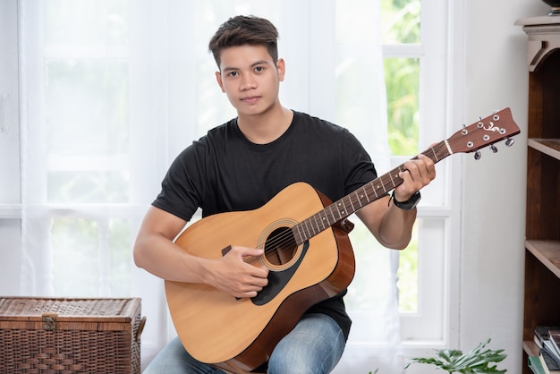 A man sitting and playing guitar on a chair.