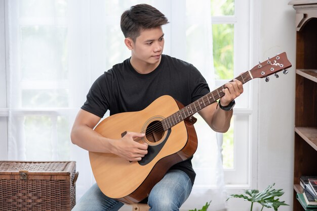 앉아서 의자에 기타를 연주하는 남자.