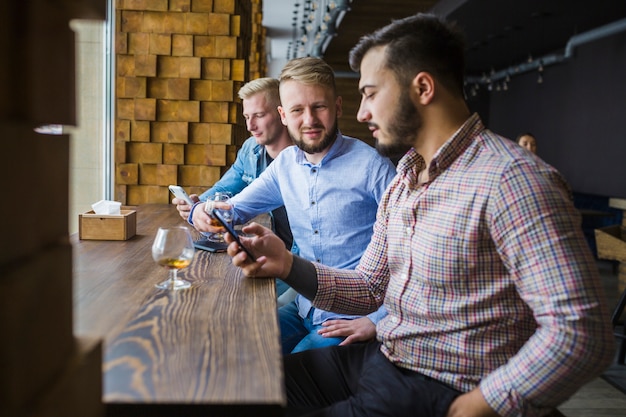 Free photo man sitting in restaurant with his friends using mobile phone