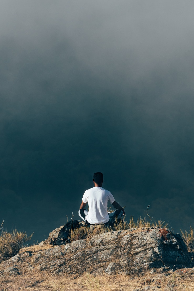 मुफ़्त फोटो man sitting on a rock