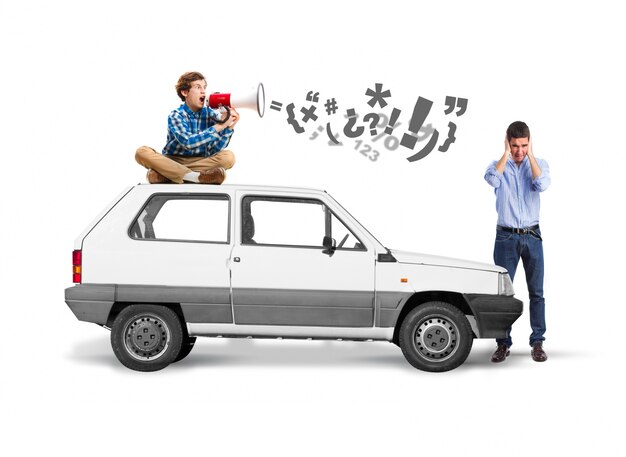 Man sitting on the roof of a car with a megaphone and another covering his ears