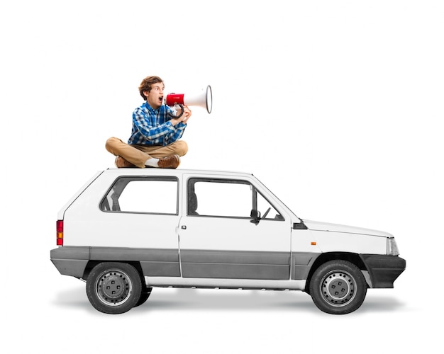 Free photo man sitting on the roof of a car with a megaphone screaming