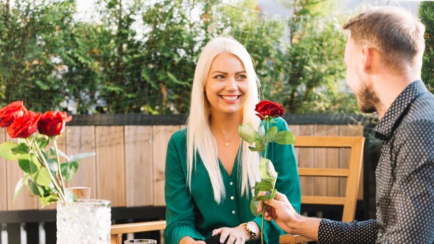 Man sitting at rooftop giving red rose to her smiling girlfriend