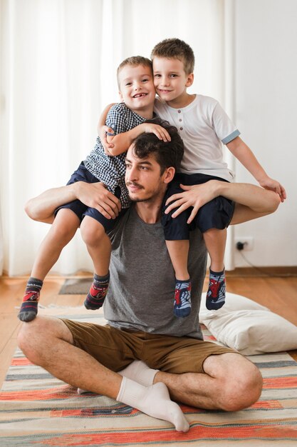 Man sitting on rug carrying his two sons on shoulder