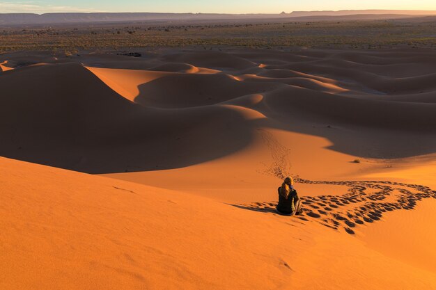 사막의 트랙으로 둘러싸인 모래 언덕에 앉아 있는 남자