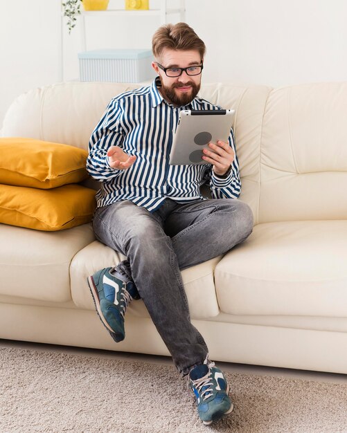 Человек сидит на диване у себя дома с планшета