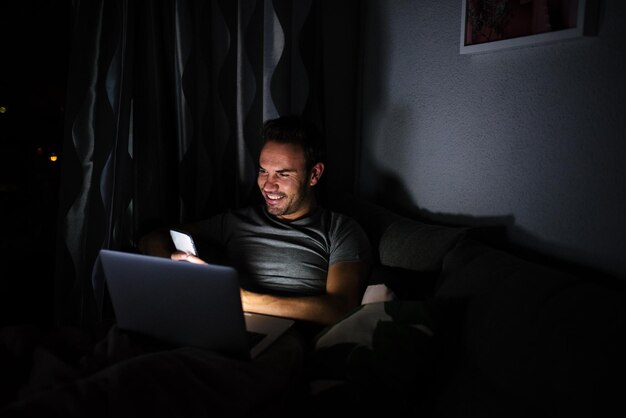 Мужчина сидит на диване с мобильным телефоном и компьютером