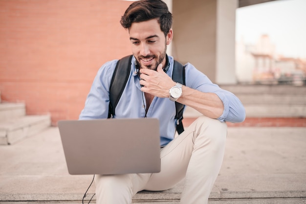 Free photo man sitting on staircase using laptop