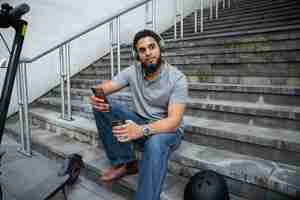 Free photo man sitting on stairs with headphones full shot