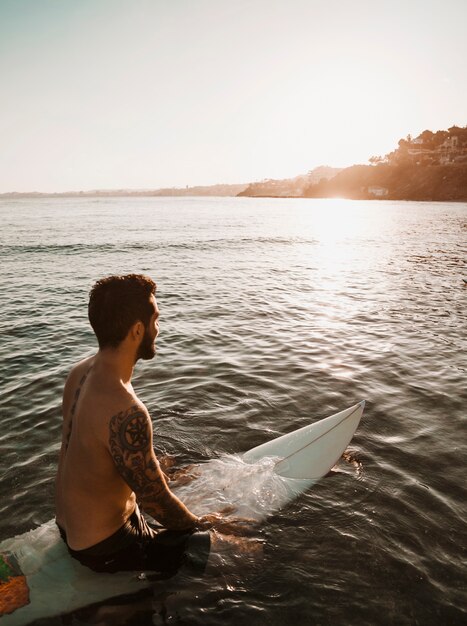 Man sitting on surfboard in water 