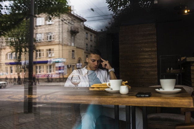 Man sitting at table in restaurant seen from window glass