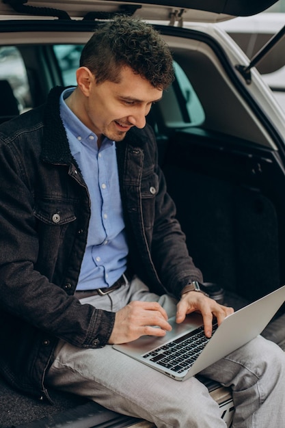 Man sitting in trunk of his car and working on computer