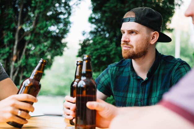 Человек, сидевший со своим другом, держащий коричневую бутылку пива