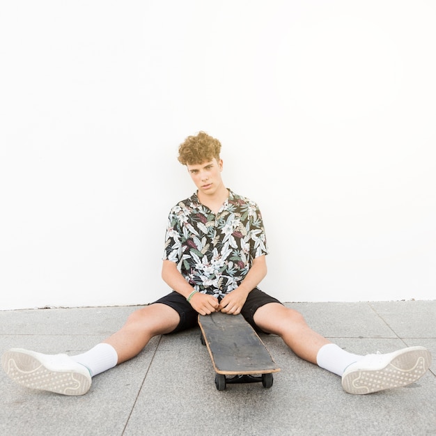 Man sitting with his leg apart sitting with skateboard