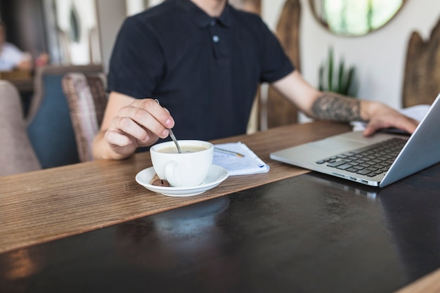Человек, сидящий с ноутбуком и кофе за столом