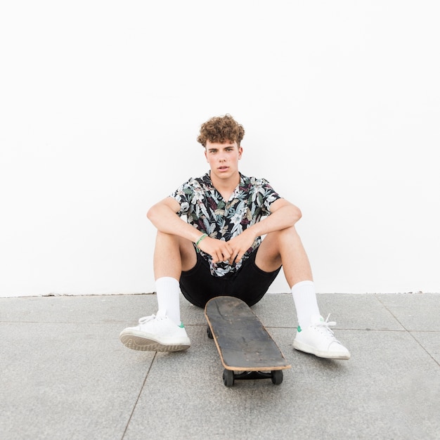 Foto gratuita uomo seduto con skateboard contro il muro