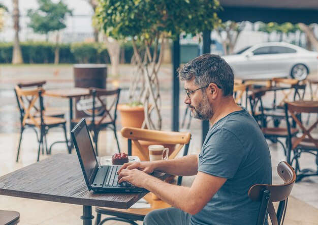 man sitting and working on laptop in cafe terrace during daytime and looking busy