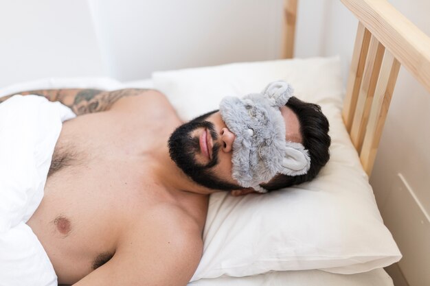 Man sleeping on bed with sleep mask