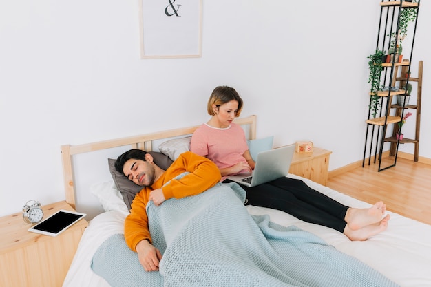 Man sleeping near woman with laptop