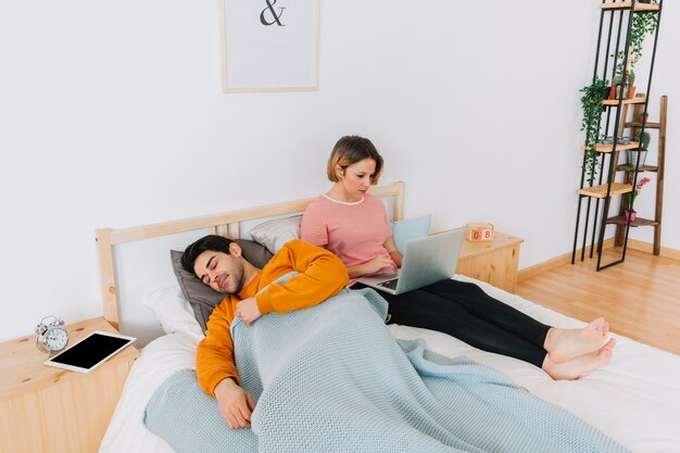 Man sleeping near woman with laptop