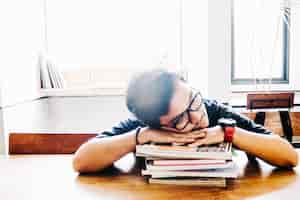 Free photo man sleeping on stack of books