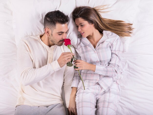 Free photo man smelling rose in bed with woman