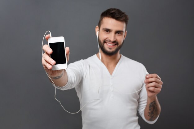 Man smiling stretching phone screen  over grey wall