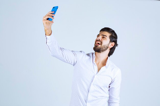 Man smiling and taking his selfie with a blue smartphone