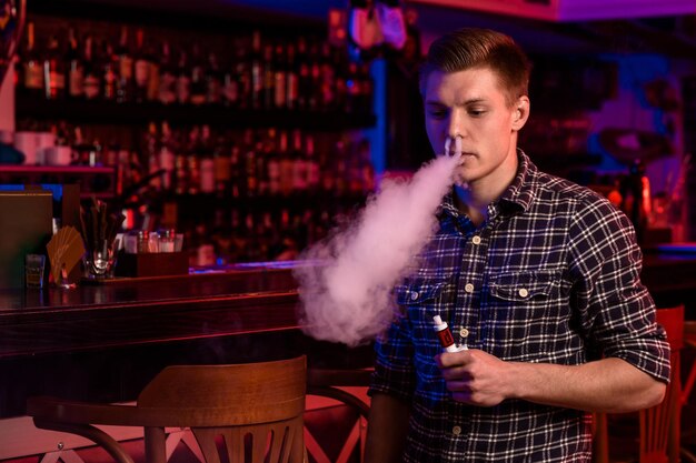 The man smoke an electronic cigarette at the vape shop. Vape bar.