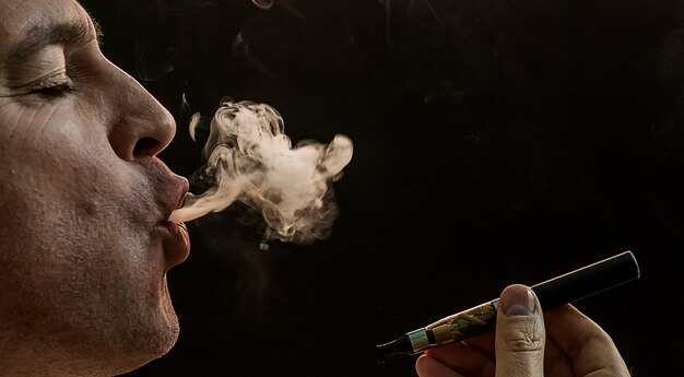 黒の背景に男の喫煙のタバコ、ハンサムな若い男の喫煙のタバコ、葉巻と黒背景に煙とミステリーの男
