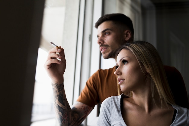 Man smoking cigarette looking out from window with her girlfriend