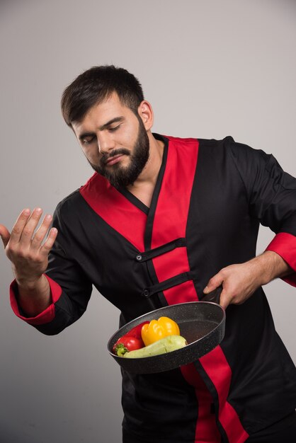 Man sniffs vegetables on dark pan .