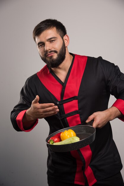 Man sniffs vegetables on dark pan .