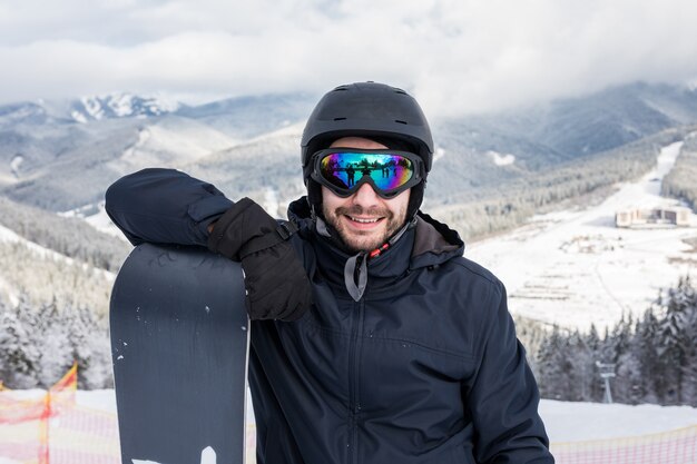 Man snowboarder stands with snowboard. Closeup portrait.