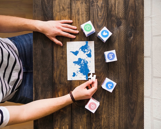 Man solving world map jigsaw puzzle near blocks of social networking icons