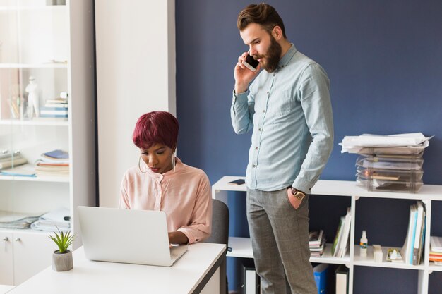 Man speaking on phone near working woman