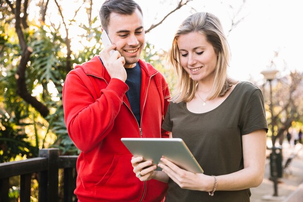 Man speaking on phone while using tablet with woman