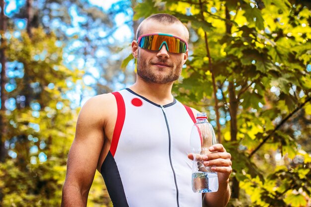 Man in sportswear and sunglasses holding bottle with water.