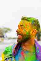 Free photo man stained paint powder with rainbow flag smiling on street
