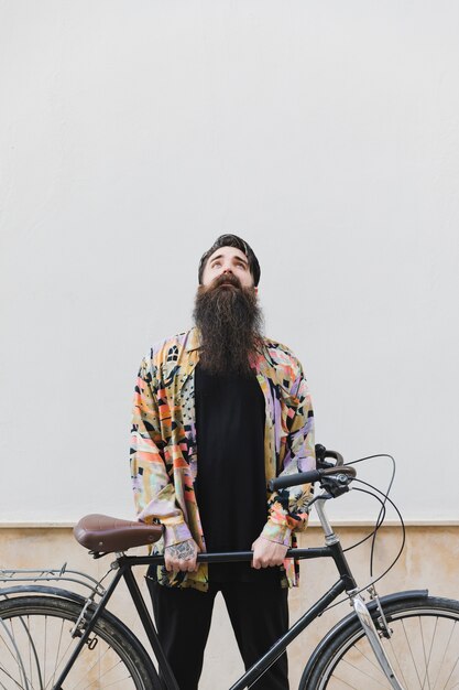 Man standing against wall holding bicycle looking up